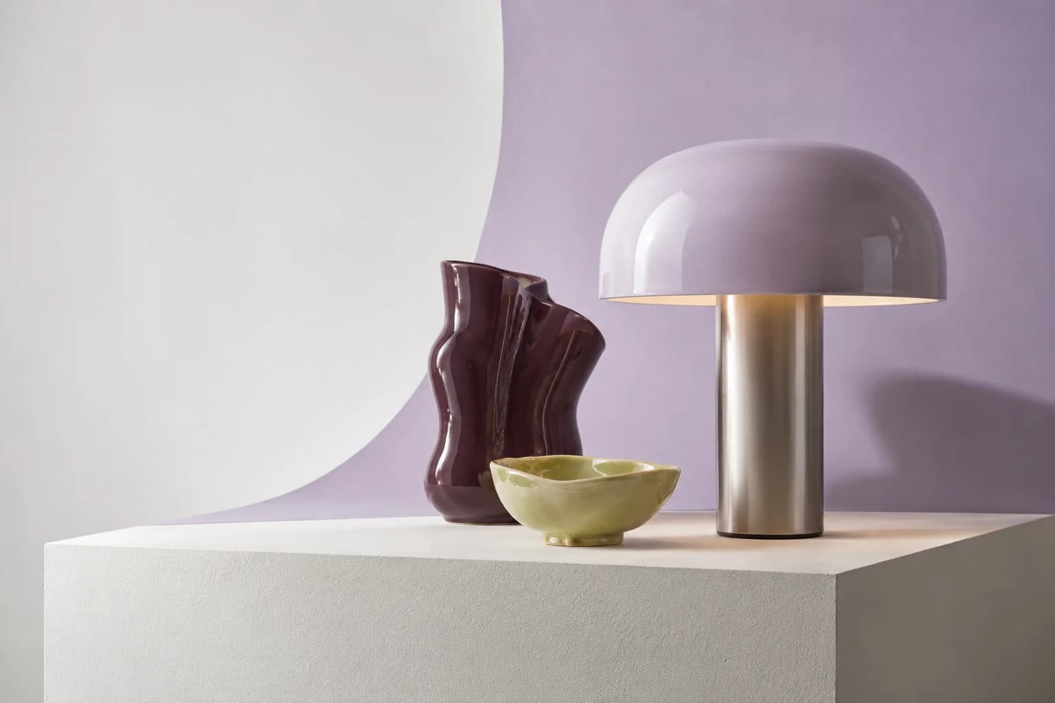 Produktstillleben mit fliederfarbener Lampe, auberginefarbener Vase und grüner Schale